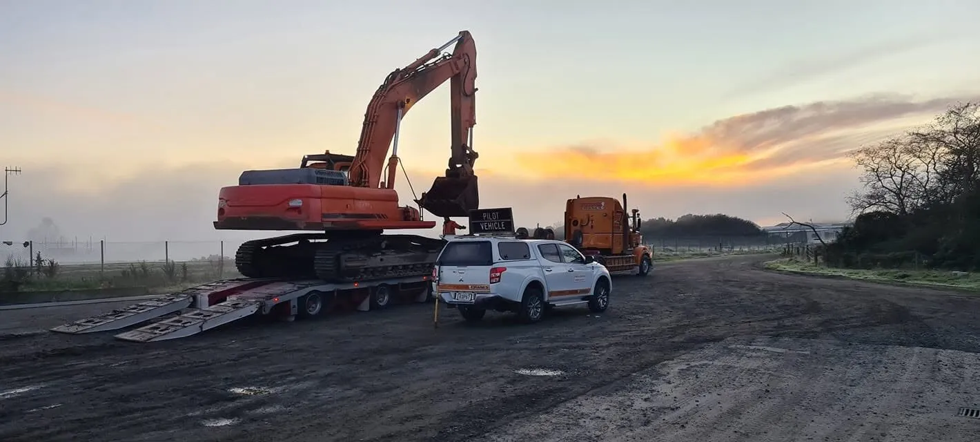 Excavator on a transporter with a pilot vehicle at sunrise